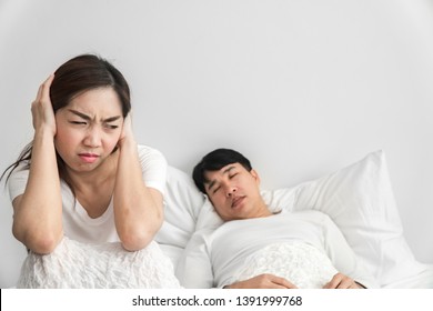 Snoring Asian Man And Young Asian Young Woman. Couple Sleeping In Bed. Young Girl Can't Sleep Because Of Her Man's Snoring. Man Snoring While His Wife Is Covering Ears With Two Hand And Very Angry.