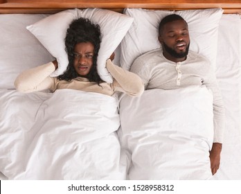 Snoring Husband. Unhappy Black Woman Covering Her Ears With Pillow, Can Not Handle Loud Snore Of Her Partner, Top View