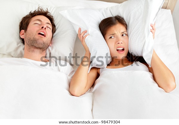 Snoring\
man. Couple in bed, man snoring and woman can not sleep, covering\
ears with pillow for snore noise. Young interracial couple, Asian\
woman, Caucasian man sleeping in bed at\
home.
