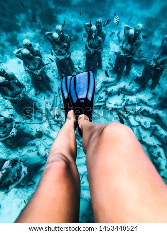 Snorkel womans legs swimming in a turquoise ocean under the flooded statues. Life tours and outdoor water sports. The concept of free diving.