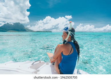 Snorkeling from boat in Bora Bora, Tahiti, French Polynesia. Woman jumping in crystal clear water with snorkel gear in coral reef lagoon with Bora Bora landmark Mount Otemanu in background.