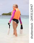 Snorkeling on the reef. Girl standing on the white sand above the blue sea water and holding swimming flippers in his hand. Fins, vacation.