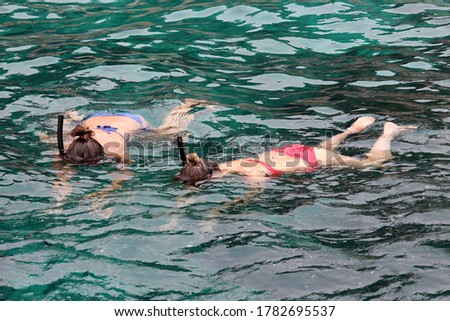 Snorkeling in the sea, beach vacation. Two girls in masks and bikini swim over a coral reef