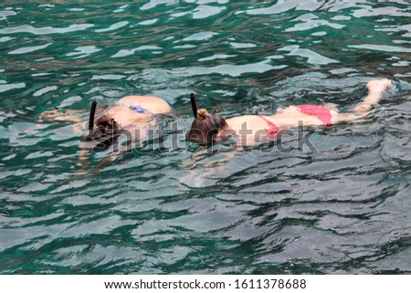 Snorkeling in the sea, two girls in masks and bikini swim over a coral reef