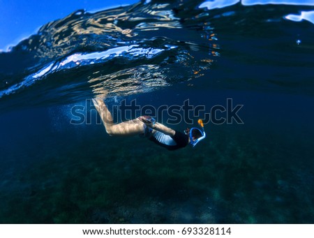 Snorkeling woman dives to sea bottom. Snorkeling girl in full-face snorkeling mask. Under waterline. Snorkel undersea. Seashore underwater photo. Active seaside vacation. Water sport in tropical sea