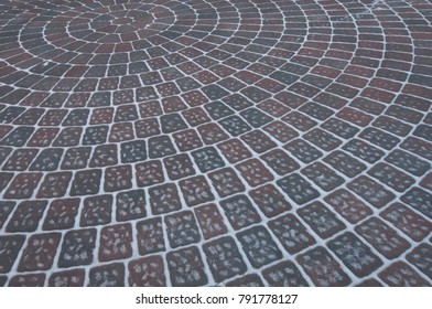 Snow Adds To Circular Design Pattern Of Sidewalk Made Of Gray And Maroon Concrete Brick Pavers