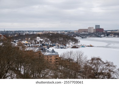 Snow blankets the waterfront of Stockholm, creating a serene winter landscape. Colorful boats are docked amidst the ice, while buildings provide a backdrop on this chilly day. - Powered by Shutterstock