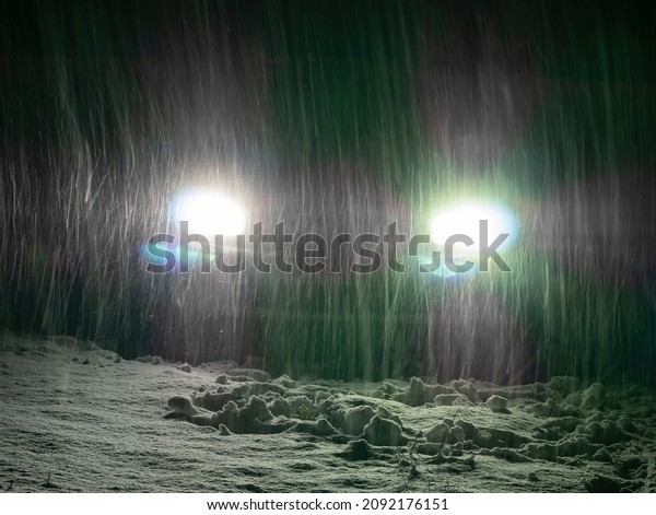 Snow\
blizzard in the light of car headlights on the night road. Falling\
white snow. Car headlights. Night automobile road. Winter season.\
Ice on the track. Frosty weather. Driving in\
winter.