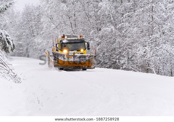 A snow\
blower car clears snow in the forest from the road on a winter\
morning. Snow plow truck cleaning icy white\
road