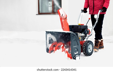 Snow blower powered by gasoline in action. Man outdoor in front of house using snowblower machine. Snow removal, thrower assistant in winter outside home. Young worker guy blowing snow during blizzard