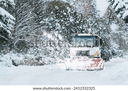 Snow is blowing out of the plow of snow remover. Snowplow truck on a snowy road in action. Plowing winter road