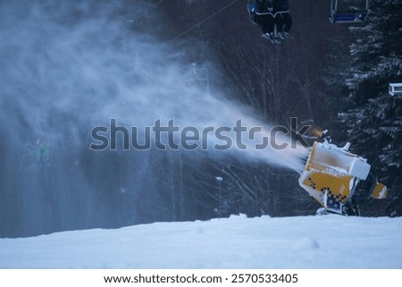 Snow cannon in the evening. Snow making machine on ski slope in the evening to prepare the mountain ski resort for the next day. Winter sports industry.