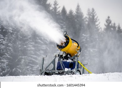 Snow cannon machine producing artificial snow on ski slope, preparation for winter season in mountain resort with forest background.