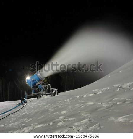 Snow cannon spraying artificial snow on a ski slope, night panorama at long exposure, closeup.