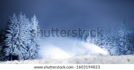 Snow cannons at night on a forest road in the background of snowy trees