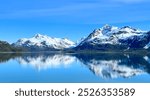 Snow capped mountains reflect off a calm ocean in Glacier Bay National Park, Alaska.