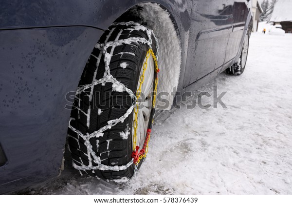 Snow chains mounted on front car tire in\
winter conditions with snow track and\
ice.