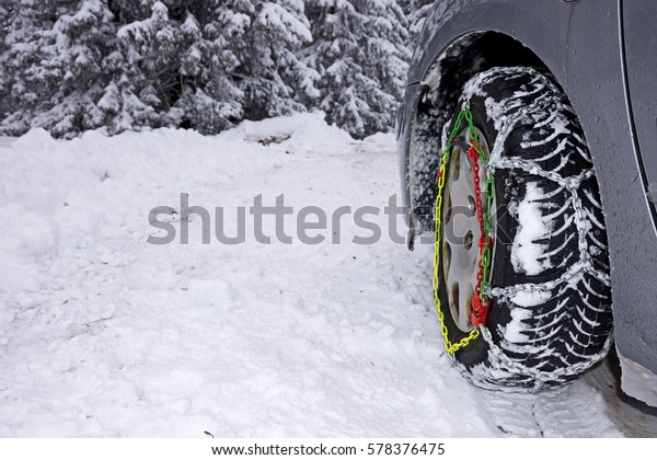 Snow chains mounted on front car tire in
winter conditions with snow track and
ice.