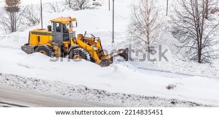 Snow clearing. Tractor clears the way after heavy snowfall. A large orange tractor removes snow from the road and clears the sidewalk. Cleaning roads in the city from snow in winter.