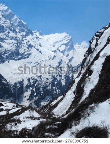 Snow covered alpine mountains and deep valley with rugged cliffs under clear blue sky, dramatic winter landscape with pristine high altitude scenery.