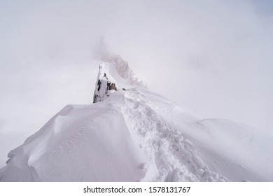 Snow Covered Alpine Ridge In Fog And Extreme Bad Weather. Alpine Mountian Landscape In Winter.