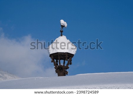 a snow covered antique weathercock on a roof at a sunny and cold winter day                 