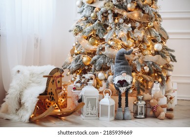 Snow Covered Artificial Christmas Tree with Golden Christmas Toys. Wooden Children's Horse. Christmas Decor Gnome under Tree.
