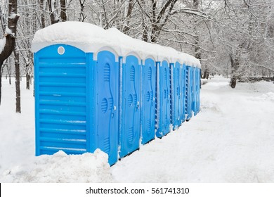 Snow covered blue portable plastic bio toilets in the park at winter 