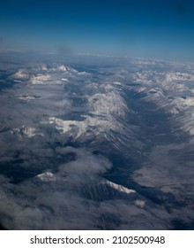 Snow Covered Canadian Rocky Mountains Viewed From Airplane Window Flying Over The Rockies In November High Snow Covered Peaks With Low Lying Clouds Making Shadows As Seen From Above In Transit In Air