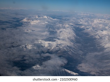 Snow Covered Canadian Rocky Mountains Viewed From Airplane Window Flying Over The Rockies In November High Snow Covered Peaks With Low Lying Clouds Making Shadows As Seen From Above In Transit In Air