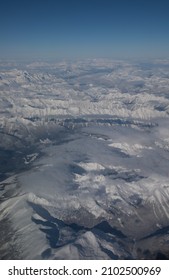 Snow Covered Canadian Rocky Mountains Viewed From Airplane Window Flying Over The Rockies In November High Snow Covered Peaks With Low Lying Clouds Making Shadows As Seen From Above In Transit In Air