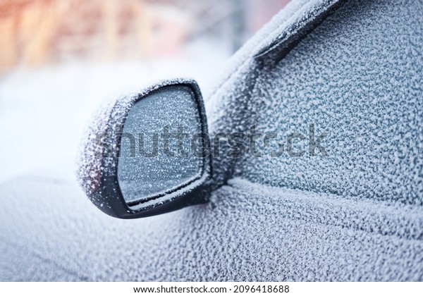 Snow covered car parked outside. Close-up of\
frozen rear view mirror.