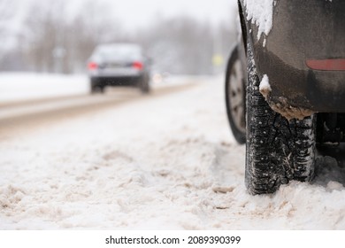 Snow covered car with studded wheels parked by the side of the road on a cold winter day