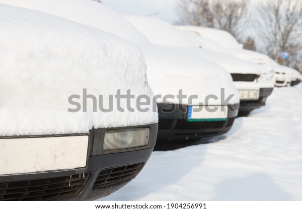 Snow covered cars parked in a row next to\
each other. Cars on the street in cold\
winter.