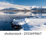 Snow covered coast of Norwegian fjord near Troms at Christmas time. A sunny winter day in Northern Norway above the Arctic Circle