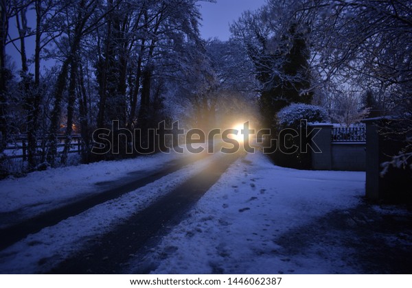 Snow Covered Country Road with Glowing Headlight
at Sunset