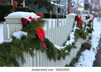 Snow Covered Evergreen Garland Draped Along A White Picket Fence