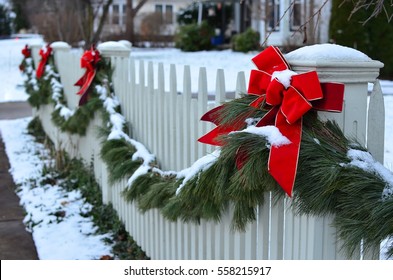 Snow Covered Evergreen Garland Draped Along A White Picket Fence