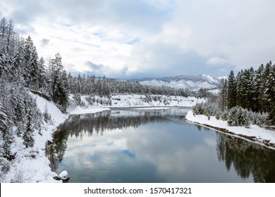 Snow Covered Evergreens Overlooking A Cold River.