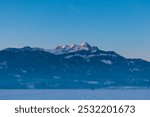 Snow covered field with panoramic sunrise view of snow-capped mountain peak Mittagskogel (Kepa) in Karawanks seen from Rosental, Carinthia, Austria. Peaceful alpine landscape. Austrian Alps in winter