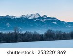 Snow covered field with panoramic sunrise view of snow-capped mountain peak Mittagskogel (Kepa) in Karawanks seen from Rosental, Carinthia, Austria. Peaceful alpine landscape. Austrian Alps in winter