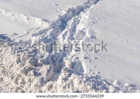 A snow covered field with a path through it. The path is cut through the snow and is the only visible sign of life in the otherwise desolate landscape
