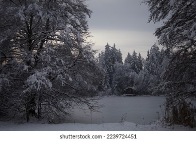 Snow covered forest in front of a frozen lake with a little fishing cabin - Powered by Shutterstock
