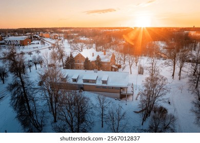 Snow covered ground during sunset with a red brick building, a modern flat roof structure, leafless trees, and additional buildings in the background. - Powered by Shutterstock