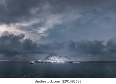 A snow covered mountain and icebergs rising from the arctic sea in Svalbard, Arctic Circle, with dark and moody sky.