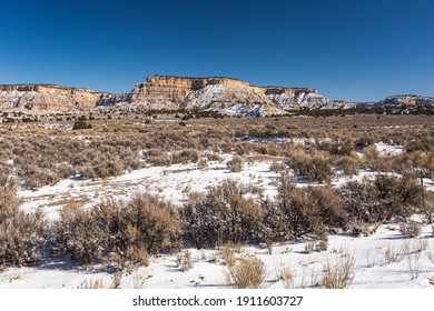 Snow Covered Mountains Behind Wide Open Desert Vista Covered In Snow With Brush On Clear Day In Rural New Mexico