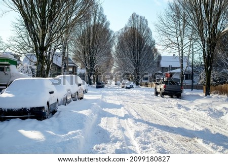 Snow covered residential street after heavy snow fall over night. Early sunny morning with blue sky. Street is not plowed and many parked cars covered with snow. Vancouver, British Columbia, Canada. 