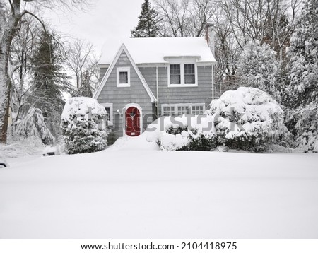 Snow covered suburban gray cottage bungalow style two story home with icicles hanging in northeastern USA winter storm