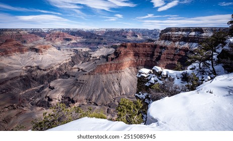 Snow covers the edge of the Grand Canyon, highlighting rock formations and contrasting with the reds and browns of the canyon walls. Clear blue skies and scattered clouds stretch over the landscape. - Powered by Shutterstock