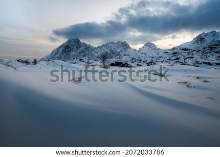 Snow dunes against the background of mountains. Scandinavian dramatic landscape. Cloudy evening on the Lofoten Islands. Textures on the snowy hills.